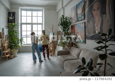 Happy glad couple of artists in love speak about art looking at paintings hanging at home apartments 117664202