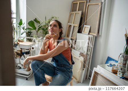 Happy thoughtful woman painter at art creative workshop workplace looking up with enthusiasm. Happy thoughtful woman painter at art creative workshop workplace looking up with enthusiasm. 117664207