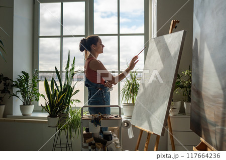 Positive optimistic woman painter embodies creative ideas expresses bright emotions in picture. Positive optimistic woman painter embodies creative ideas expresses bright emotions in picture. 117664236