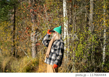 Enthusiastic woman with binoculars, studying birds and watching nature in sunny autumn woodland 117664444