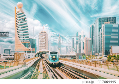 Metro road among glass skyscrapers in Dubai. Metropolitan railway among modern glass skyscrapers in Dubai. Traffic on street in Dubai. Urban background. Altered sky Metro road among glass skyscrapers in Dubai. Metropolitan railway among modern glass skyscrapers in Dubai. Traffic on street in Dubai. Urban background. Altered sky 117664445