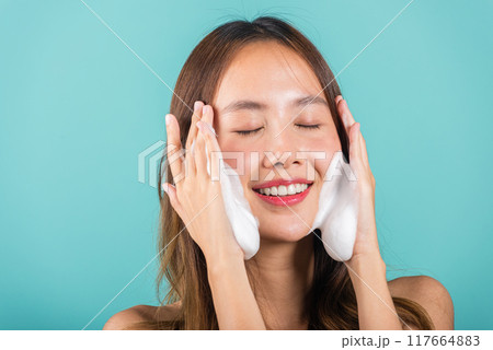Portrait beautiful female smile applies foaming cleanser healthy skin, Asian women face wash exfoliating scrub soap with skincare cleansing, Studio isolated on blue background, skincare daily routine 117664883