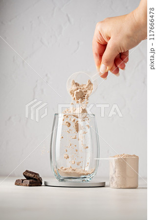 Protein powder in a scoop. Pouring chocolate protein powder in a glass. Food supplement. Protein powder in a scoop. Pouring chocolate protein powder in a glass. Food supplement. 117666478