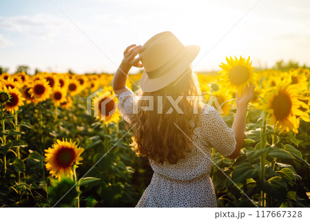 Beautiful woman strolling through field with sunflowers. Fashion, lifestyle, vacations concept. 117667328