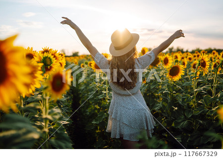 Beautiful woman strolling through field with sunflowers. Fashion, lifestyle, vacations concept. 117667329