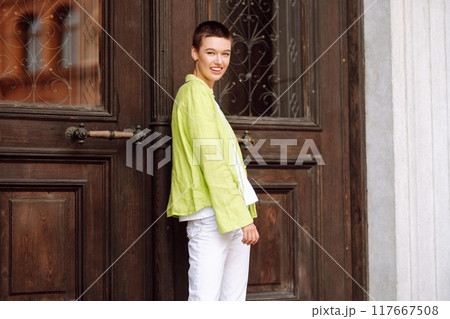 Positive woman with a short haircut and a green shirt walks and relaxes on the streets of the city. Positive woman with a short haircut and a green shirt walks and relaxes on the streets of the city. 117667508