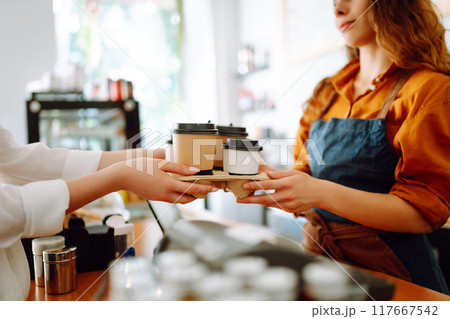 Close-up of a female barista's hands passing prepared drinks to go. Concept of orders to go. Close-up of a female barista's hands passing prepared drinks to go. Concept of orders to go. 117667542