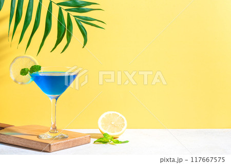 Blue summer cocktail with lemon and palm leaf 117667575