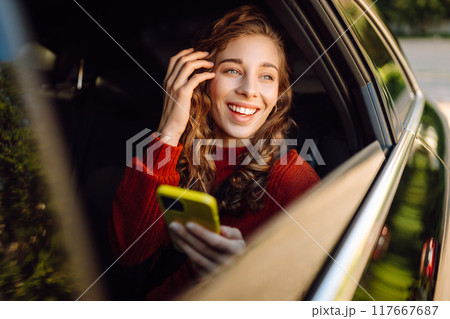 Positive young woman in casual clothes sits in the back seat of a car with a mobile phone. 117667687