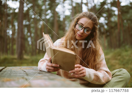 Happy woman is sitting at table with book in beautiful forest. Concept of relaxation, lifestyle. Happy woman is sitting at table with book in beautiful forest. Concept of relaxation, lifestyle. 117667788