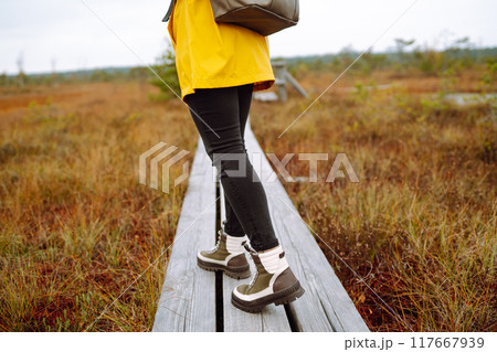 Close-up of legs in boots of woman tourist walking along wooden path against backdrop of wildlife Close-up of legs in boots of woman tourist walking along wooden path against backdrop of wildlife 117667939