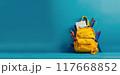 Yellow schoolbag on empty blue background. Orange bag with stationery and school accessories. Child backpack for learning 117668852