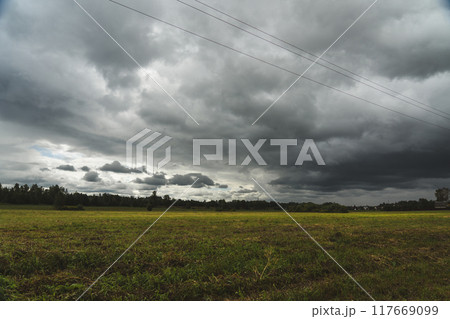 Clouds hung over the village and the green field. Support of power lines nearby Clouds hung over the village and the green field. Support of power lines nearby 117669099