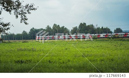 A high-speed electric train travels along a green field. A train in the distance A high-speed electric train travels along a green field. A train in the distance 117669143