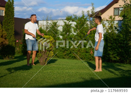 Father and son playing badminton together in a sunny backyard in summer Father and son playing badminton together in a sunny backyard in summer 117669593