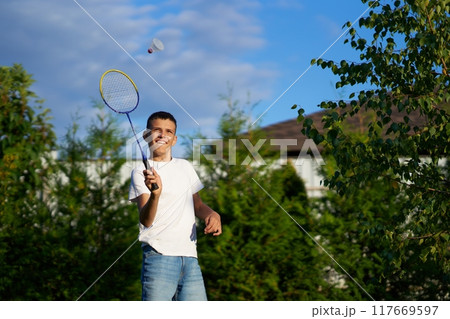 Boy playing badminton outdoors in a sunny backyard with trees 117669597