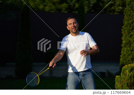 Man playing badminton outdoors in a garden during late afternoon Man playing badminton outdoors in a garden during late afternoon 117669604