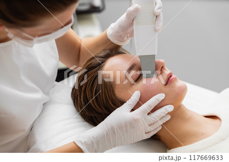Aesthetician performing facial treatment on a client in a modern skincare clinic Aesthetician performing facial treatment on a client in a modern skincare clinic 117669633