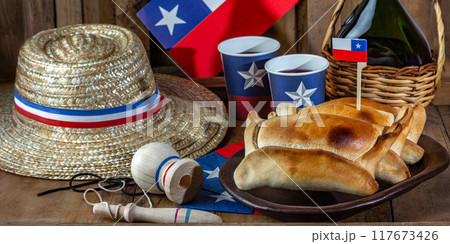 Chilean independence day concept. fiestas patrias. Tipical baked empanadas de pino, wine or chicha, hat and play emboque. Dish and drink on 18 September party, wooden background 117673426