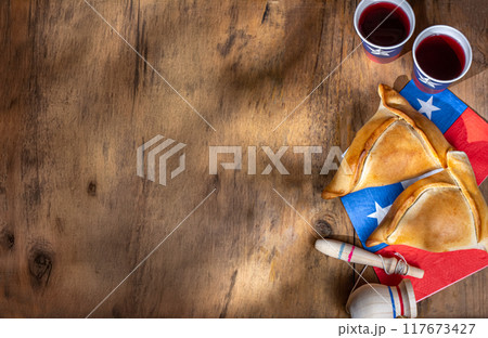 Chilean independence day concept. fiestas patrias. Tipical baked empanadas, wine or chicha, fat and play emboque. Decoration for 18 september party day, wooden background, top view 117673427