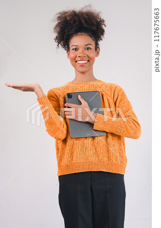 Smiling African American woman holds a tablet in one hand and points upward in a presentation gesture. Isolated on a white background. 117675663