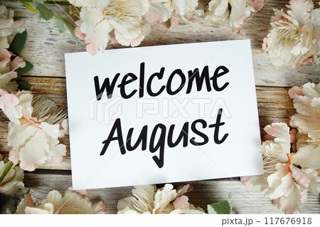 Welcome August text on paper card with flowers frame top view on wooden background 117676918