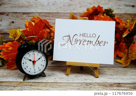 Hello November text with alarm clock and maple leaf decoration on wooden background 117676950