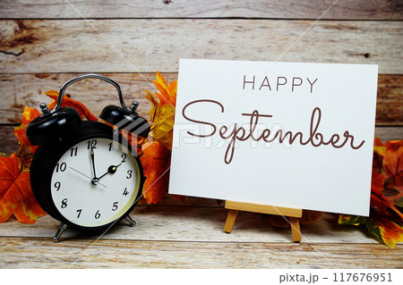Happy September text with alarm clock and maple leaf decoration on wooden background Happy September text with alarm clock and maple leaf decoration on wooden background 117676951