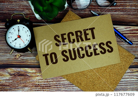 Secret to Success text written on paper torn with alarm clock top view on wooden background 117677609