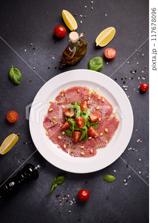 cooking tuna carpaccio - Fresh raw tuna fillet with olive oil and pine nuts on white ceramic plate 117678096