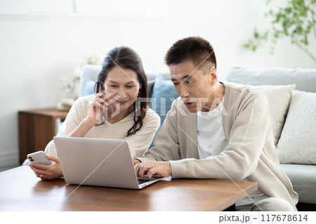 リビングでノートパソコンを使うシニア夫婦 117678614