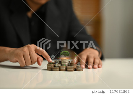 Businessman pointing at a pile of coins with a small tree. Long term investment, Interest rate and financial growth concept Businessman pointing at a pile of coins with a small tree. Long term investment, Interest rate and financial growth concept 117681862