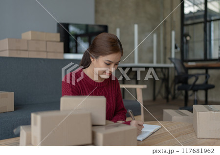 woman, online seller, using a notebook efficiently manages customer orders and delivery through the e-commerce platform 117681962