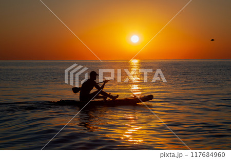 Silhouette of a man floating on a board with an oar. Dawn sun on the sea. Swimming on a supboard. Water active sports. Beautiful landscape. Sunset on the sea. Ocean coast. Copy space. 117684960