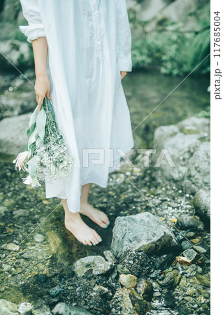 白いワンピースで夏の川に入っている女性の足元と花束 117685004