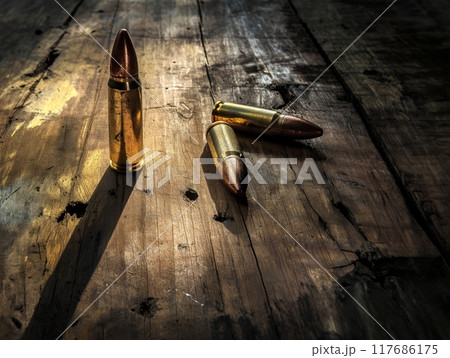 Three bullets rest on a weathered wooden surface, illuminated by dramatic lighting, casting long shadows. 117686175