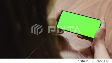 Young woman sitting at a table and using a smartphone with horizontal green screen Young woman sitting at a table and using a smartphone with horizontal green screen 117688148