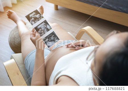 pregnant woman holds an ultrasound photo of her baby, smiling as she gazes at the image. The ultrasound shows a clear picture of the developing baby, capturing a precious moment of motherhood pregnant woman holds an ultrasound photo of her baby, smiling as she gazes at the image. The ultrasound shows a clear picture of the developing baby, capturing a precious moment of motherhood 117688821