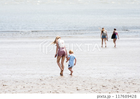 遠浅の砂浜を歩く金髪の親子　南ウェールズの郊外の海岸にて 117689428