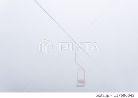 chair of chairlift over mountain slope in cloudy weather 117690042