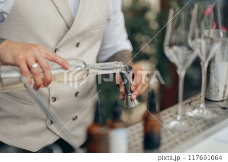Bartender making a cocktail, pouring vodka from a bottle into a cocktail measuring cup, adding all the ingredients into shaker Bartender making a cocktail, pouring vodka from a bottle into a cocktail measuring cup, adding all the ingredients into shaker 117691064