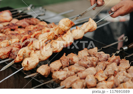 Frying shish kebab on the skewers in brazier. Fresh ruddy meat for barbecue grill on fire outdoor. 117691089