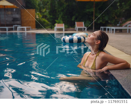 Vacation lifestyle scene of young woman sitting in swimming pool Vacation lifestyle scene of young woman sitting in swimming pool 117691551