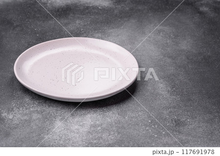 Empty ceramic plate on a dark textured background Empty ceramic plate on a dark textured background 117691978