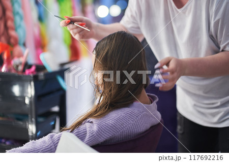 The master combs the girl's hair before braiding braids. There is a defocused kanekalon hair material in the background. With space to copy. High quality photo The master combs the girl's hair before braiding braids. There is a defocused kanekalon hair material in the background. With space to copy. High quality photo 117692216