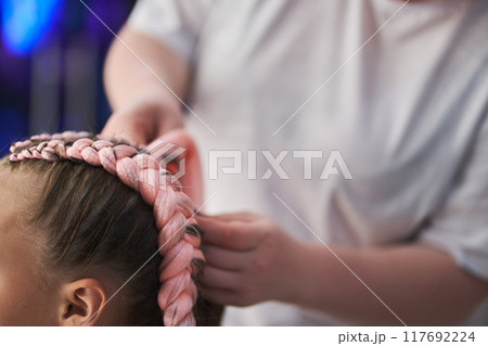 Close-up of the pigtail on the child's head made of pink kanekalon. The hands of the master who weave the kanekalon material into the hair. With space to copy. High quality photo Close-up of the pigtail on the child's head made of pink kanekalon. The hands of the master who weave the kanekalon material into the hair. With space to copy. High quality photo 117692224
