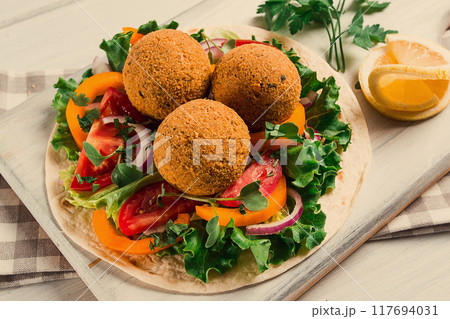 Tortillas, wrapped falafel balls, with fresh vegetables, vegetarian healthy food, on a wooden white background, no people, selective focus. 117694031