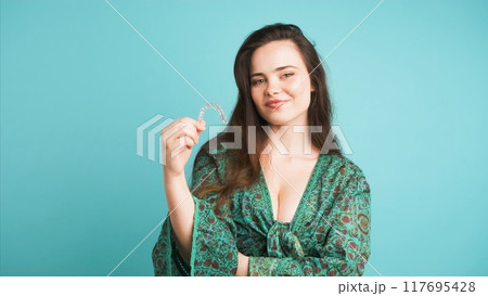 Happy young woman showing invisible braces in blue studio 117695428
