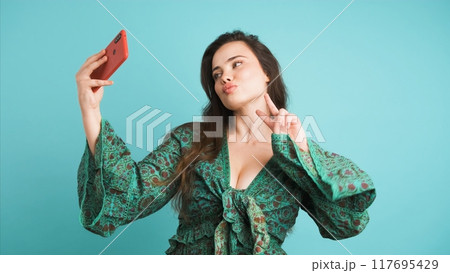 Happy woman taking selfie with smartphone in blue studio Happy woman taking selfie with smartphone in blue studio 117695429