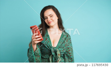 Smiling young woman using smartphone in blue studio 117695430